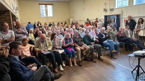 A meeting of residents in Bramley shows a room full of attendees and some standing around the edges of the hall