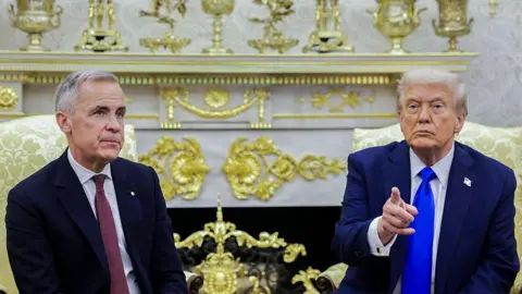 US President Donald Trump, right, and Mark Carney, Canada's prime minister, during a meeting in the Oval Office of the White House in Washington, DC, US, on Tuesday, Oct. 7, 2025. Trump is wearing a suit with a bright royal blue tie and is gesturing with his finger. Carney is wearing a suit with a burgundy tie and has a neutral expression on his face.
