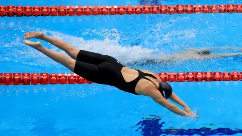 Susannah Next dari Inggris mengambil bagian dalam final S5 gaya bebas 50m putri pada hari pertama Kejuaraan Renang Dunia Paralimpiade di London Aquatics Centre, mengenakan baju renang hitam dengan celana pendek dan topi renang hitam.