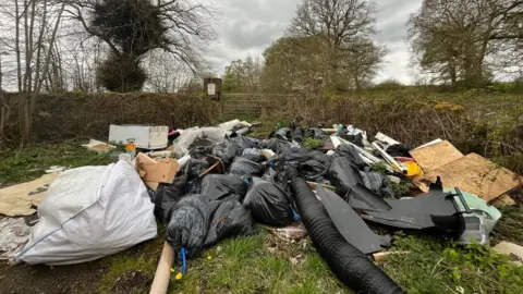 A big pile of rubbish including black bin bags, cardboard and tubing.