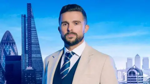 A close up shot of Phil Turner wearing a jacket and tie looking to camera with a London skyline backdrop