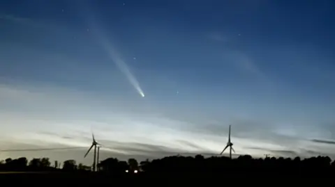 Skyborg/BBC Weather Watchers Comet A3 above two wind turbines and trees.