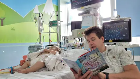 Family handout A dad reading to his baby son in hospital