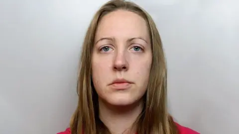 Cheshire Police Lucy Letby, with blonde hair and a red tracksuit, sits in front of a grey background