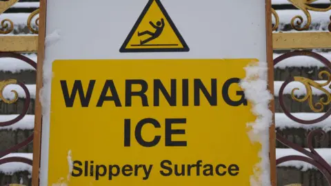 A picture of a yellow sign which reads warning ice slippery surface. 