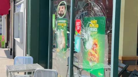 Jamie Niblock/BBC Another shop front window that has been smashed. Tables and chairs have been placed outside the business.