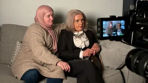 Miri de Villers Julie and Tatiana is sitting on a grey sofa and a camera is in front recording them