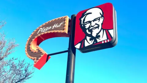 Getty Images A sign with an arrow pointing to Pizza Hut on the left and the KFC Colonel logo on the right