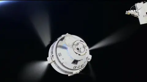 NASA The moment the capsule disconnects from the ISS and begins its journey to Earth. The capsule has a round bottom, which narrows into a cone shape. The section of the ISS which it was attached to can also be seen in the picture, with the expanse of space visible in the background. In this image three beams of light can be seen coming from the different sides of the capsule. 