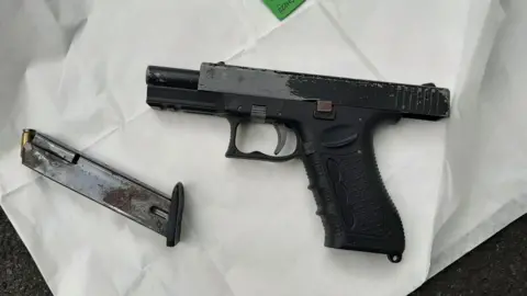 Cambridgeshire police Black handgun placed on white paper- with an ammunition magazine with a bullet showing at the top on the left.