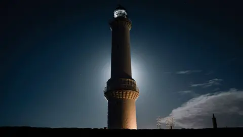 A lighthouse silhouetted against a bright moon