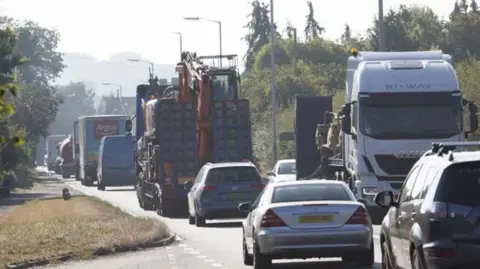 A single carriageway road completely congested with cars, vans and lorries