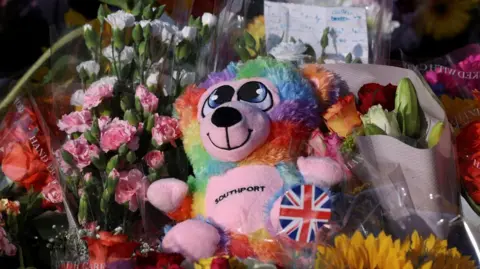 PA Media A close up of a teddy with the words Southport on its chest, surrounded by flowers