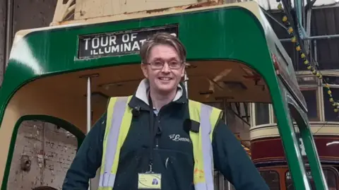 LDRS Councillor Paul Galley stands on a green-liveried tram in a workshop that has been retrofitted into a museum.