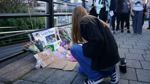 PA Media A fan looks at messages and flowers left to honour Liam Payne at the Keel Warf Bridge at Royal Albert Dock in Liverpool