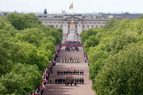 PA Media An aerial view shows groups of military in formal attire marching down the Mall with Buckingham Palace in the background.
