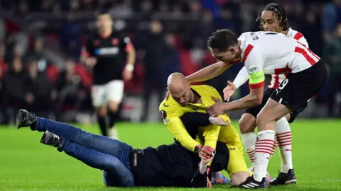 A pitch invader interacts with Sevilla FC goalkeeper Marko Dmitrovic