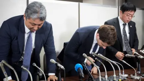 Getty Images Mark Karpeles (centre) bows at a press conference after appearing in court.