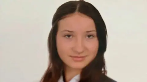 A school photo of Scarlett Vickers smiling into the camera. She has dark, long hair with a centre parting and dark eyes.