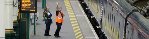 PA Media Train staff wave off a train on an empty platform at Waverley Station in Edinburgh