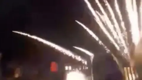 fireworks shooting across a dark sky in front of houses