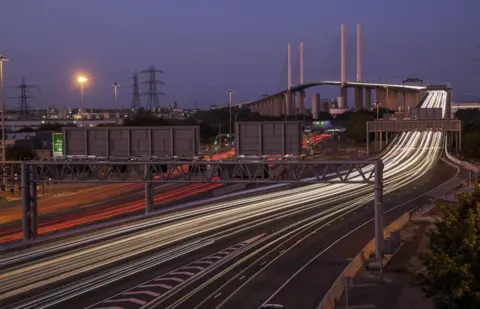 Getty Images A view of the Queen Elizabeth II Bridge at night. There are two separate light trails from vehicles travelling over the bridge, one red from the back lights of vehicles, the other white, from their headlights.