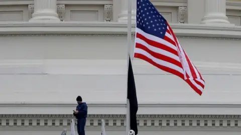 Reuters A worker walks under an American flag flown at half staff at the US Capitol