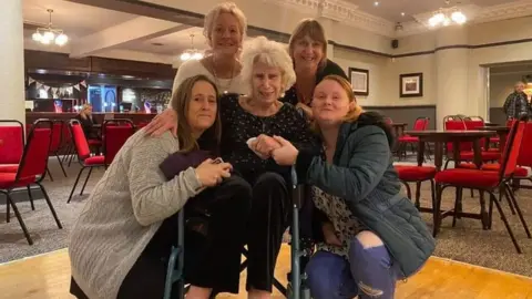 Tanglewood Care Services Ltd Liliana Scott on the dance floor in the wheelchair surrounded by family and friends