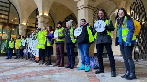 Umbrella Fair Line of campaigners wearing hi-biz and carrying slogans at Northampton Guildhall