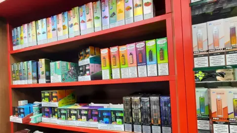 Red shelving with a colourful array of packaging for vapes.