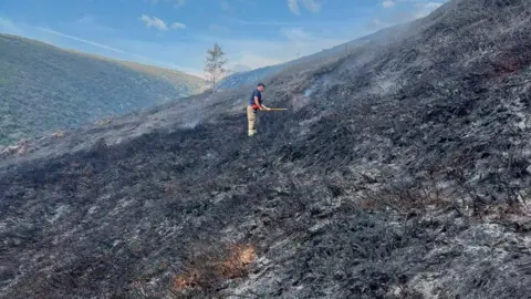 Derbyshire Fire and Rescue Service A firefighter damping down hot spots following a moorland wildfire on Tintwistle Moor, above Woodhead Road in Glossop, Derbyshire.