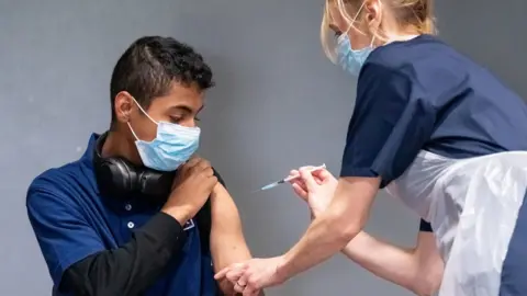 PA Media Nurse Sonia Wilson (right) vaccinates eighteen-year-old Cameron Ladd (left) with the Pfizer Covid-19 vaccination, at a mass coronavirus vaccination centre at Adwick Leisure Centre, in Doncaster