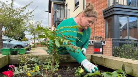 Woman gardening in a wooden planter filled with soil and a green plant.