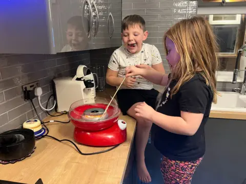 Family handout This is a photo of Rory and Mya when they were younger. Two children - a boy aged about eight and a girl aged about five - are in the kitchen of their home. The girl is mixing what looks like cake batter on the kitchen work top, while the boy is sat on the worktop watching. The boy is in a light coloured T-shirt and black shorts, with dark hair. The girl is wearing floral leggings with a black T-short and light brown hair. 