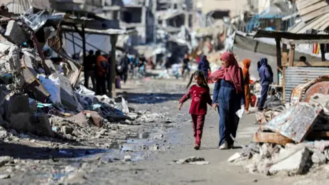 Reuters Palestinians walk past the ruins of houses destroyed during Israel's military offensive, amid the ongoing conflict between Israel and Hamas, in Gaza City, March 20, 2024