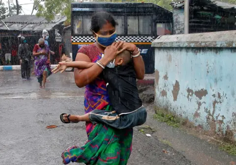 Rupak De Chowdhuri / REUTERS A woman carries her son as she tries to protect him from heavy rain
