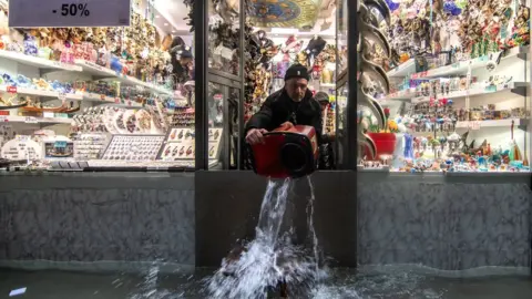 Getty Images A shopkeeper uses a bucket to remove water from his property in Venice, 13 November 2019