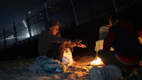 EPA An elderly man sits in front of a fire outside a tent in the city of Rafah, in the southern Gaza Strip 27 February 2024.