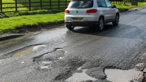 Getty Images A car driving by a series of potholes in Slough, 2023