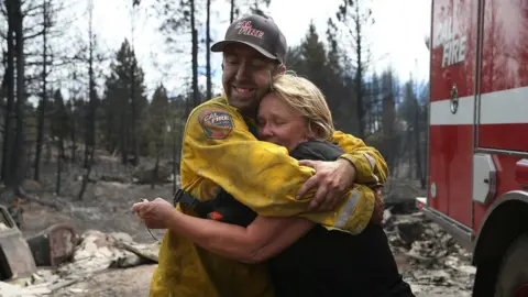 Getty Images Kathy Besk (R) hugs CalFire firefighter Tommy Janow (L) after he found three of her rings in the burned-out ruins of her home