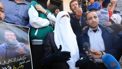 EPA Randa Mousa (C), the wife of Palestinian Islamic Jihad member Khader Adnan, speaks to journalists following his death, outside her home in Arraba, in the occupied West Bank (2 May 2022)