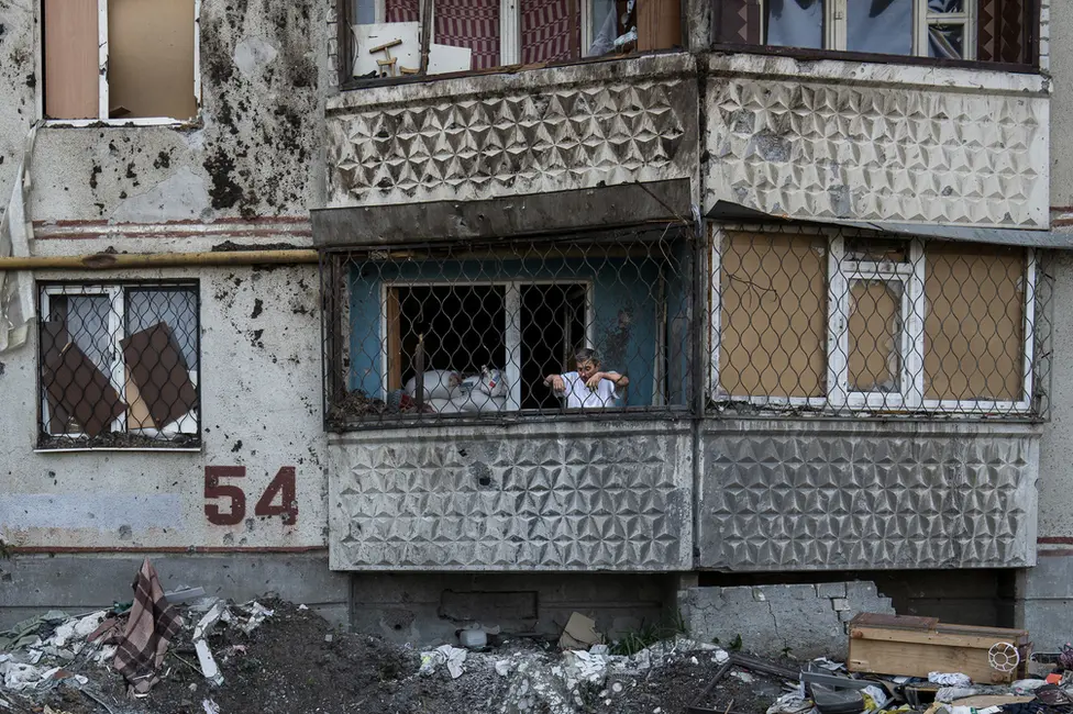 BBC A resident of Saltivka building 54 looks down from his balcony at a shell crater beneath. "This is the Russian world," he said