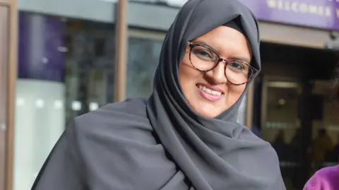 City of Wolverhampton Council Obaida Ahmed - wearing a dark grey hijab and glasses - smiles as she stands outside the City of Wolverhampton Council headquarters.