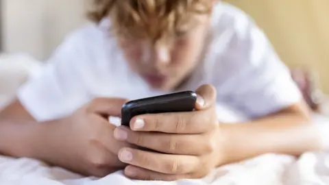 Getty Images a teen holding smart phone in bed