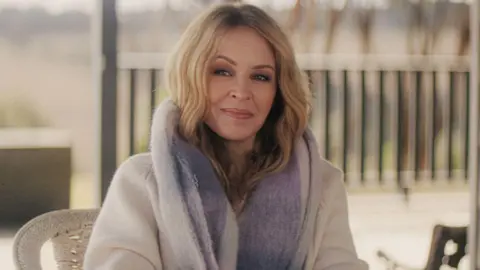 Kylie Minogue smiling at the camera while wearing a fur coat in the new three-part Netflix documentary, Kylie