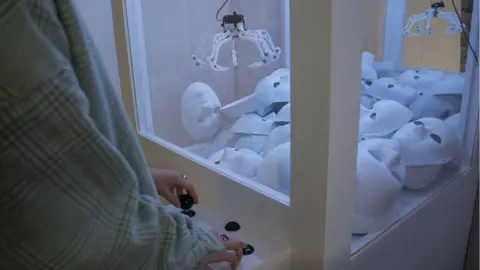 Dana Leslie claw machine with white masks as prizes