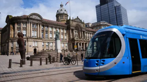 The outside of Birmingham City Council's council house, with a statue of Queen Victoria in front and a blue tram crossing in front.