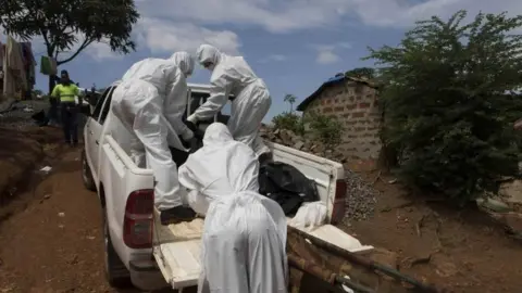 Reuters A burial team wearing protective clothing remove a body of a person suspected of having died of the Ebola virus in Freetown, Liberia (28 September 2014)