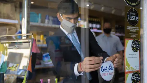 HM Treasury The Chancellor Rishi Sunak applies an "eat out to help out" sticker in a window