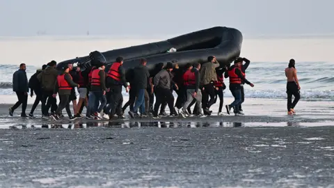 Getty Images Migrants carry a boat towards the water before they attempt to cross the Channel illegally to Britain, July 2022